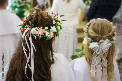 Dziewczynki stojące w kościele podczas uroczystości pierwszej komunii świętej z wiankami kwiatów na głowach
