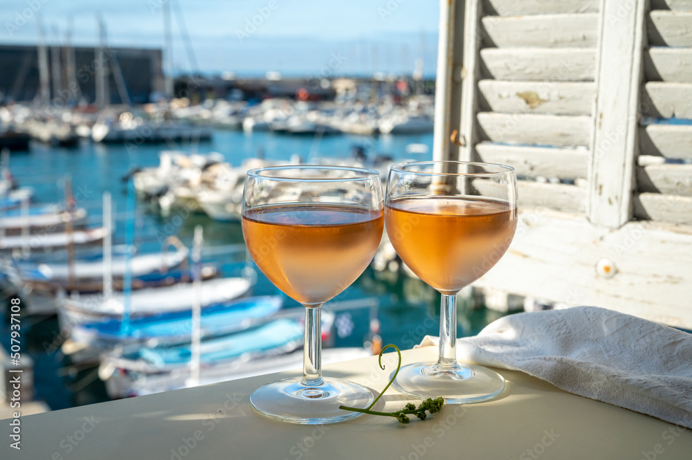Obraz premium Cold rose wine in glasses served on outdoor terrace in sunlights with view on old fisherman's harbour with colourful boats in Cassis, Provence, France