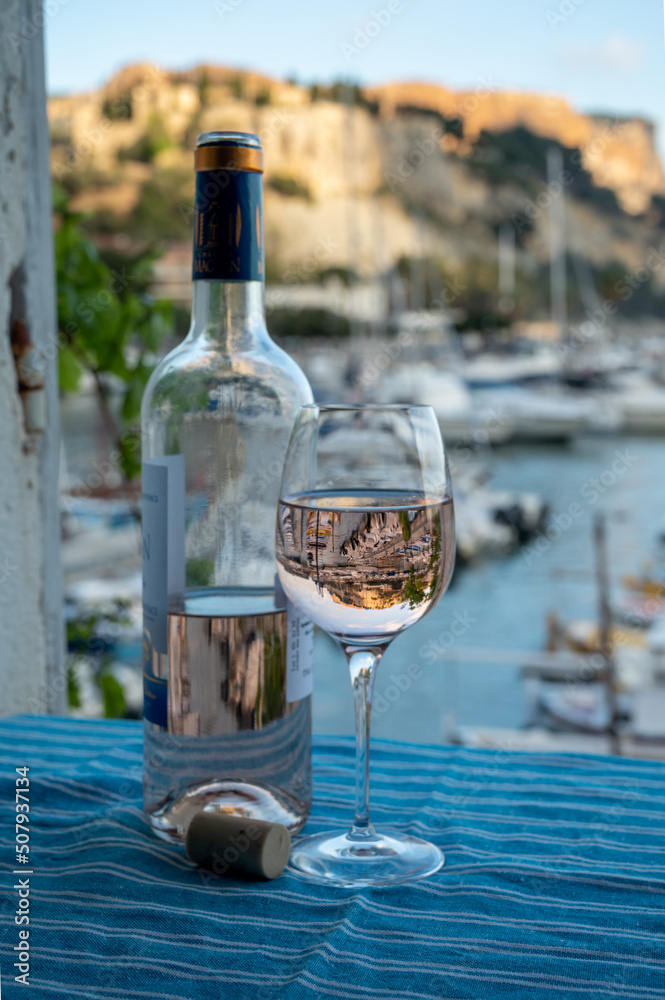 Rose wine in glass and bottle served on outdoor terrace with view on old fisherman's harbour with colourful boats in Cassis, Provence, France