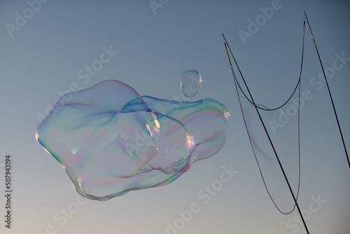 Big soap bubble. Colorful soap bubble on the blue sky. Bubble making with rope and sticks.