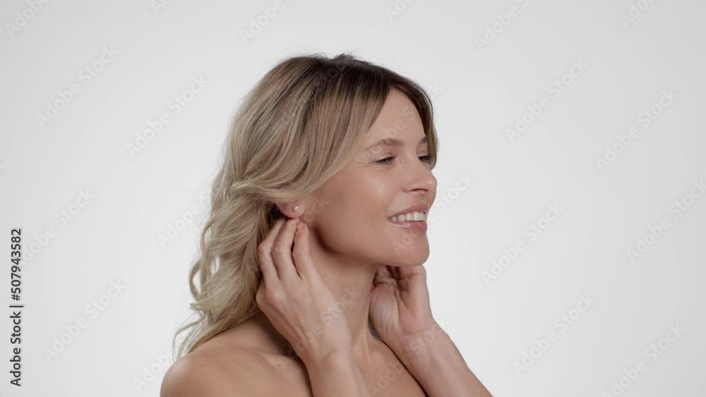 Semi profile portrait of beautiful middle aged woman with bare shoulders massaging neck, white studio background Semi profile portrait of beautiful middle aged woman with bare shoulders massaging neck, white studio background