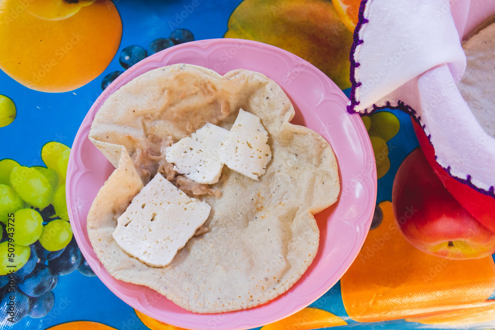 Mujer mexicana torteando maza de maíz en un metate y una estufa de leña