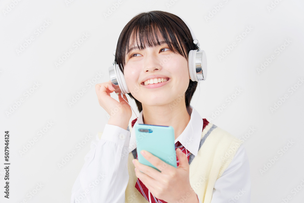 白背景でヘッドホンでスマホで音楽を聴く女子高生