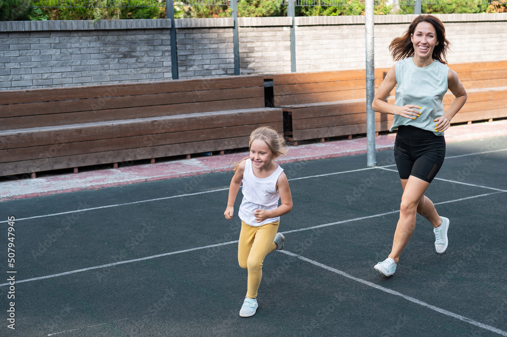 Caucasian woman goes in for sports with her daughter outdoors. A schoolgirl and her mother are running around in the stadium. Caucasian woman goes in for sports with her daughter outdoors. A schoolgirl and her mother are running around in the stadium.