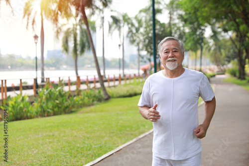 Happy and smiling asian senior man doing exercise and jogging or walking with relaxation for healthy in park outdoor after retirement during summer time. Health care elderly outdoor lifestyle concept. © feeling lucky