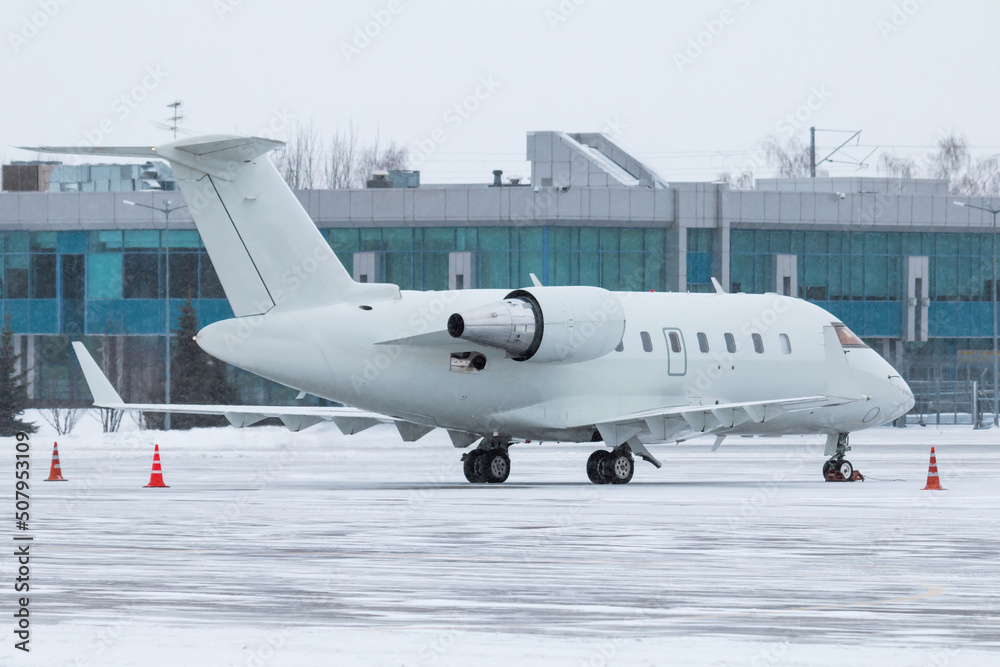 White luxury executive business jet on the winter airport apron near the terminal in a severe blizzard White luxury executive business jet on the winter airport apron near the terminal in a severe blizzard