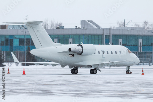 White luxury executive business jet on the winter airport apron near the terminal in a severe blizzard