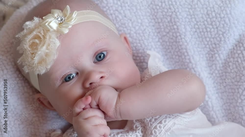 Little girl lying on a cozy bed and sucking her fingers, licks fist, looking at the camera. Baby teething concept. Little girl lying on a cozy bed and sucking her fingers, licks fist, looking at the camera. Baby teething concept.
