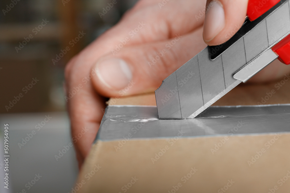 Man using utility knife to open parcel, closeup