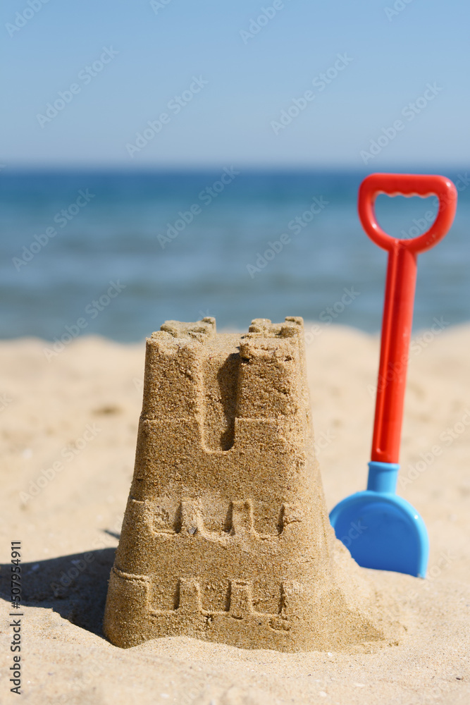 Sand castle and child plastic shovel on beach near sea Sand castle and child plastic shovel on beach near sea