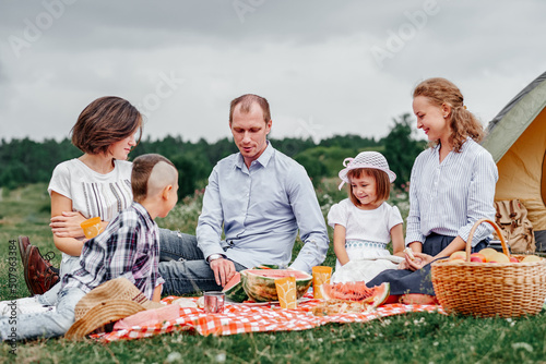 Happy family eating watermelon at a picnic. Picnic in the meadow or park. Young friends and their children in nature