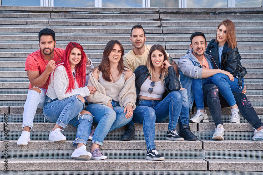 Obraz premium Group of friends smiling at the camera while sitting together on outdoor stairs. Friendship and positivity concept.