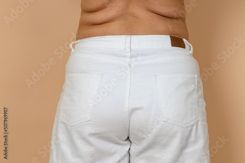 Closeup of female big waist with fat sides, love handles wearing white jeans. Body positive. Accepting who you are. Tight clothes. Need for wardrobe change.