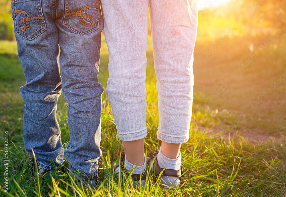 two pairs of children's legs in jeans close-up outdoors in the sun two pairs of children's legs in jeans close-up outdoors in the sun
