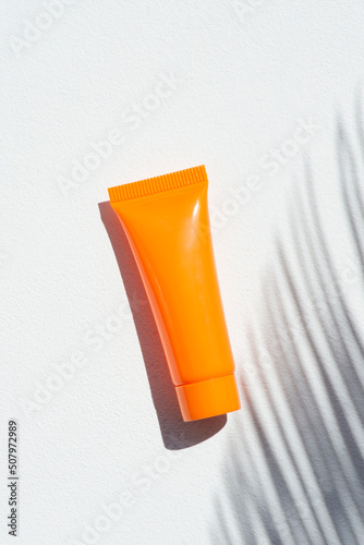 Plastic orange bottle for cream or lotion on a white background. Skincare cosmetic with beautiful palm shadows. Beauty concept for face body care