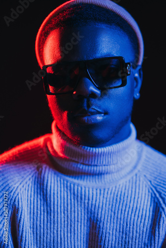 Neon light man. Night portrait. Cyberpunk fashion. Cool handsome guy face in sunglasses in bright red blue glow isolated on dark background. © golubovy
