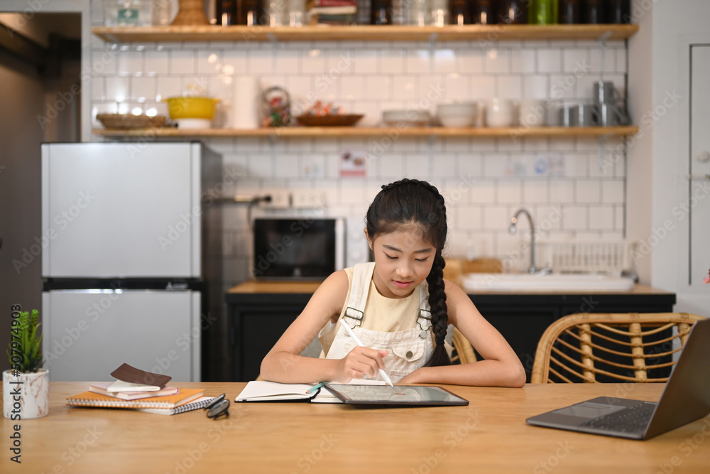 Asian girl sitting in home kitchen and using digital tablet with distance learning virtual distance online class. Education and school concept