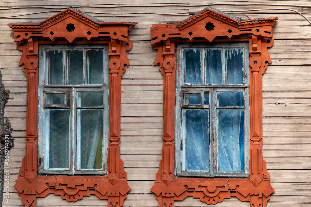 Direct view of an old wooden apartment building in Nizhny Novgorod. Windows with carved red platbands, curtains and pots of flowers on the windows, paint streaks on the glass
