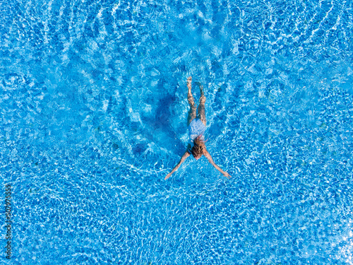 Top view of woman in swimsuit swimming in pool from above view, aerial top view from drone, summer relaxation in hotel