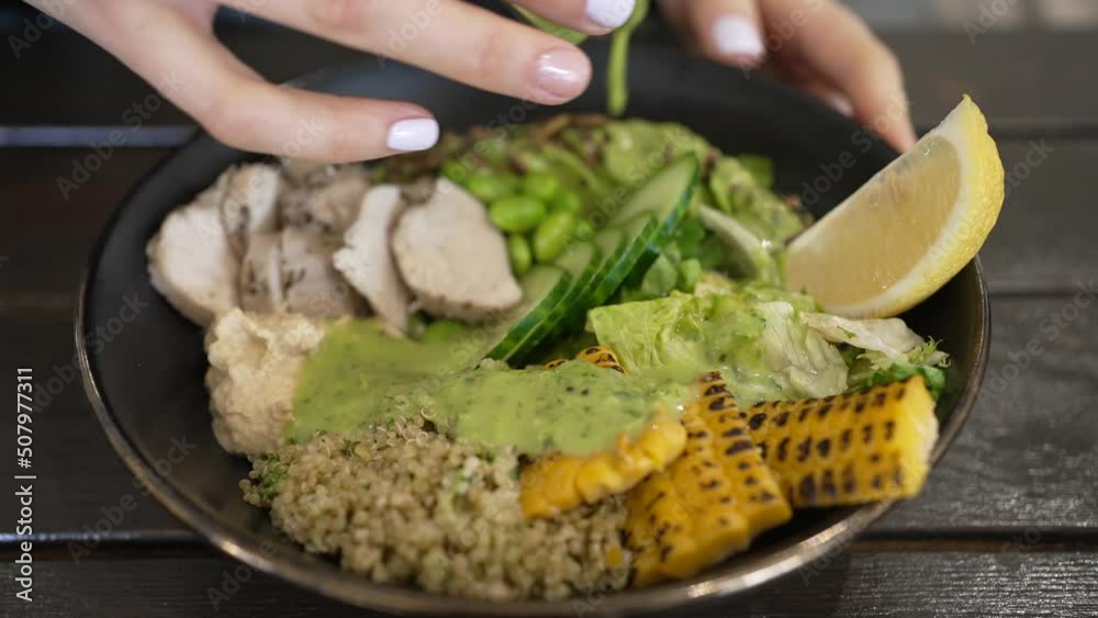 Bowl with avocado and turkey meat seasoned with guacamole salsa. Female hands in restaurant pour guacamole salsa sauce into dish closeup
