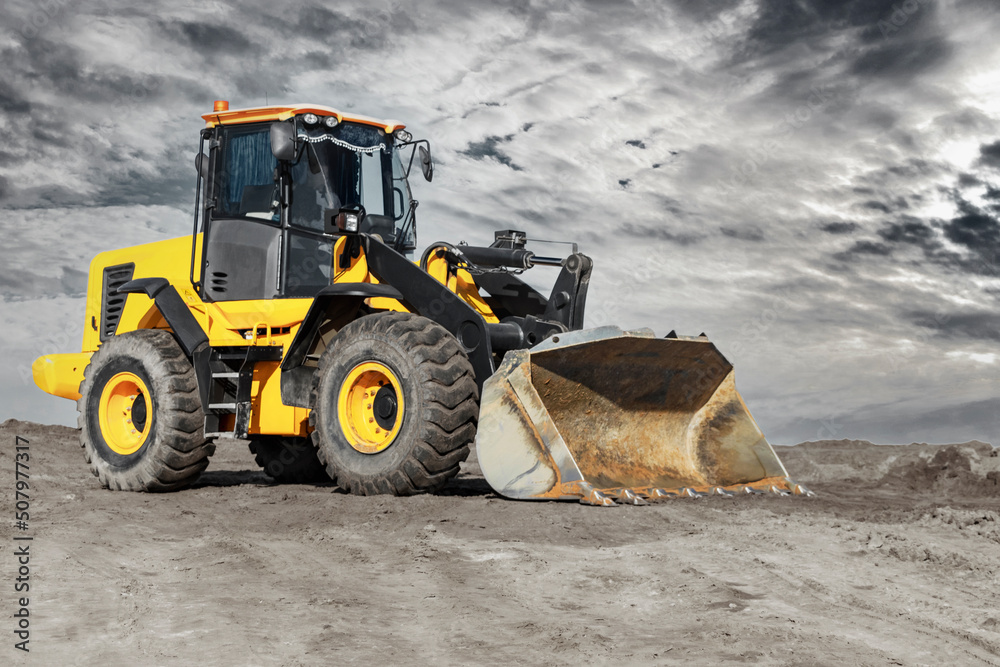 Bulldozer or loader moves the earth at the construction site against the sunset sky. Contrasting image of a modern loader or bulldozer. Construction heavy equipment for earthworks. Bulldozer or loader moves the earth at the construction site against the sunset sky. Contrasting image of a modern loader or bulldozer. Construction heavy equipment for earthworks.
