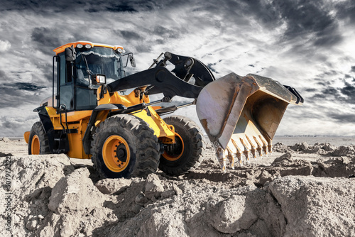 Bulldozer or loader moves the earth at the construction site against the sunset sky. Contrasting image of a modern loader or bulldozer. Construction heavy equipment for earthworks.