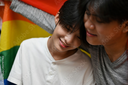 Beautiful Asian young gay man in a warm embrace of his gay boyfriend and LGBT flag.