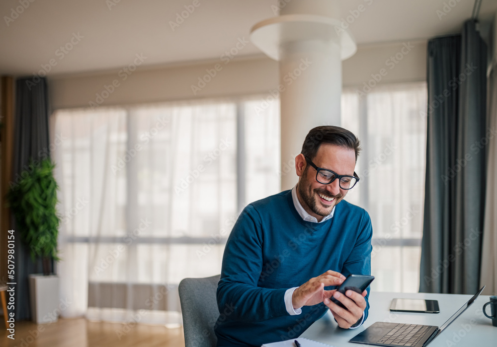 Smiling businessman networking on smart phone while sitting at corporate office