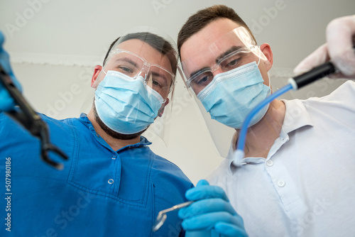 Bottom view of male dental doctor and his assistant with stomatological instrument look on patient