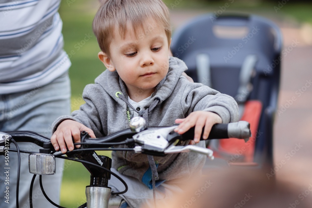 Cute little caucasian boy sitting on frame of father bicycle. Family weekend in countryside Cute little caucasian boy sitting on frame of father bicycle. Family weekend in countryside