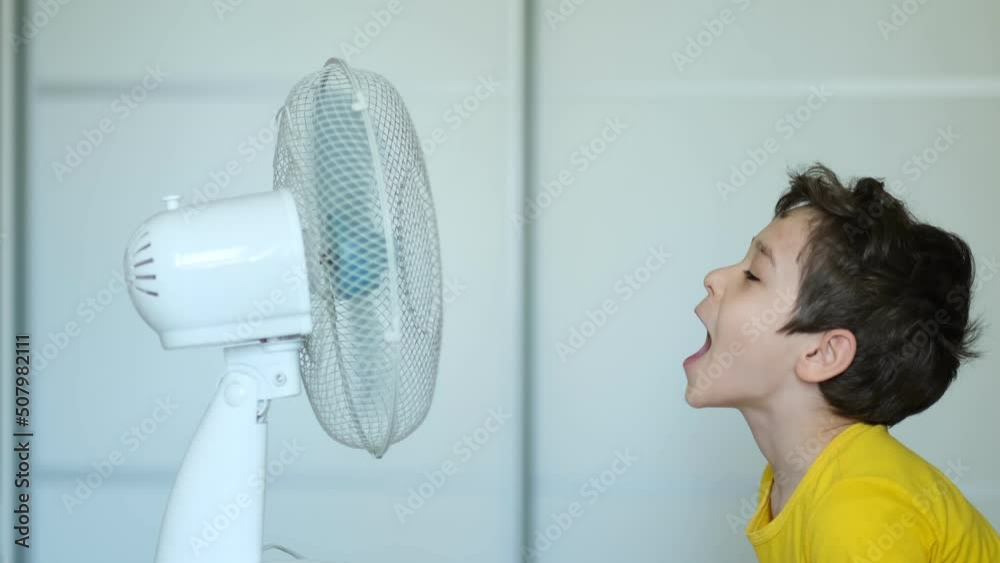preschool boy cooling in front of fan. Little child refreshing from heat in front of small fan at home. Cute small kid play with ventilator blowing cool wind alone.