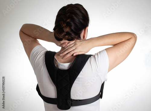 A girl in a white T-shirt wears a posture corrector on a white background. Back pain treatment concept and treatment for stooped spine. photo