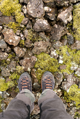 Legs in grey hinking trousers and black orange hiking boots on volcanic stones