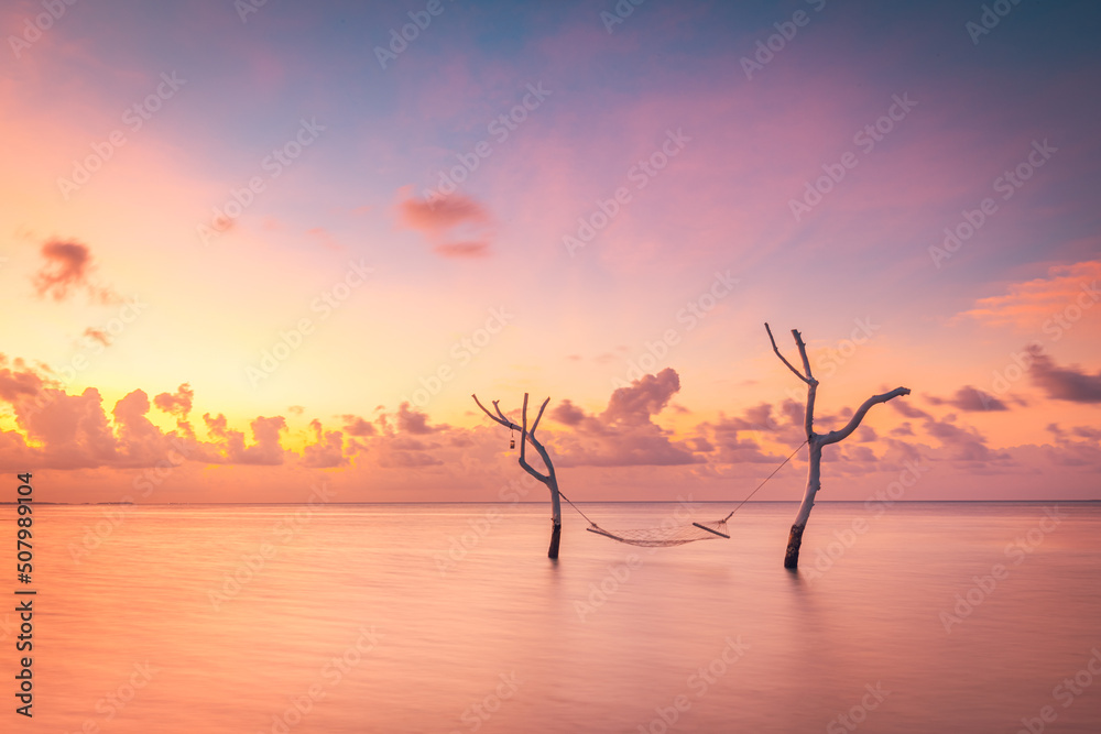 Beautiful bright sunset on a tropical paradise beach. Abstract long exposure water and sky, tree branches with swing or hammock. Amazing lagoon, island shore, relaxation, recreation leisure carefree Beautiful bright sunset on a tropical paradise beach. Abstract long exposure water and sky, tree branches with swing or hammock. Amazing lagoon, island shore, relaxation, recreation leisure carefree