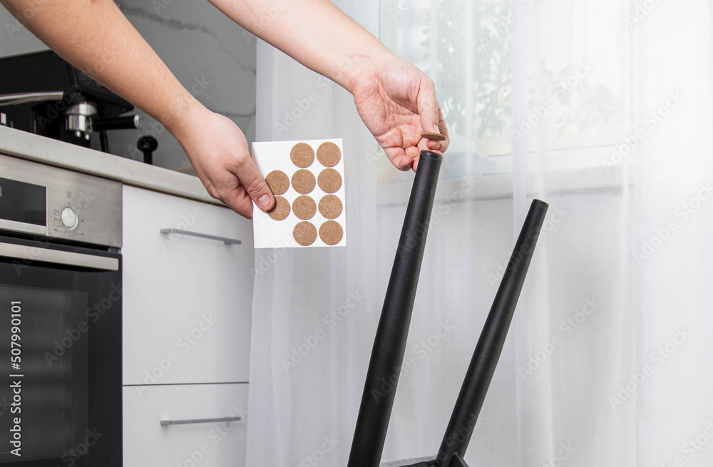 Obraz premium A man glues protective pads on the legs of a chair. Protection against floor scratches and noise