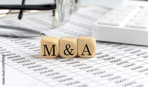 Photos wooden cubes with the word M and A on a financial background with chart, calculator, pen and glasses, business concept