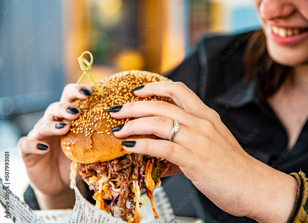 Woman eating street food burger outdoors. Traditional barbecue pulled beef burger with vegetables in woman hand