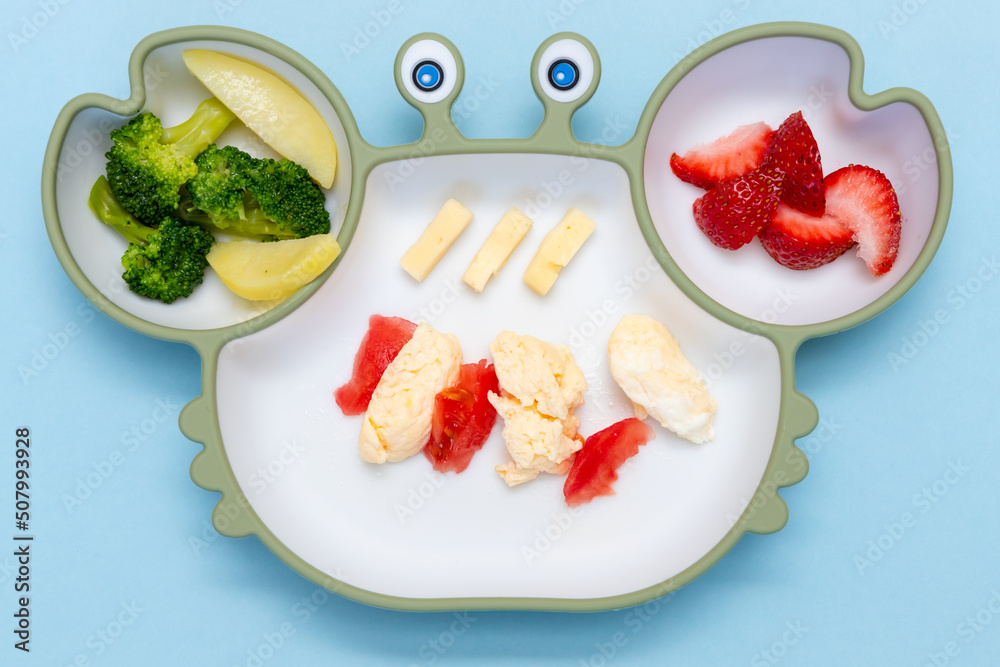 Baby Led weaning, blw. First baby food. Silicon plate with mixed vegetable. Healthy nutrition for kid, self feeding. Soft eco plastic tableware. Close up Baby Led weaning, blw. First baby food. Silicon plate with mixed vegetable. Healthy nutrition for kid, self feeding. Soft eco plastic tableware. Close up