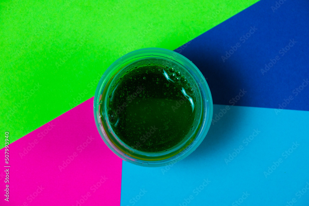 Liquid cleansing green washing gel in the dispenser on a bright, rich multicolored paper background with copy space. The concept of effective washing of clothes with color preservation.
