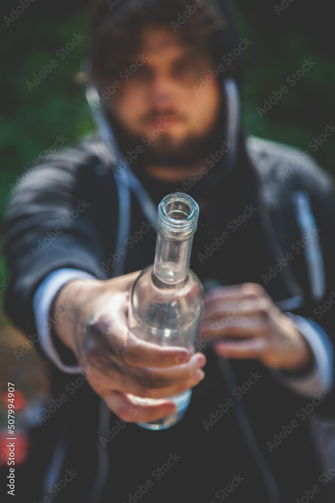 Fototapeta premium Portrait of drunk young man with a bottle of vodka. Alcoholism, pity, hopelessness, social problem of dependence concept. Vertical image.