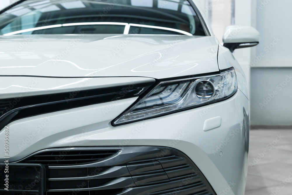 The concept of automotive detailing. Close-up of the front of the car. Close-up of car headlights. Partial view of a modern brand new white car. The front of the vehicle.