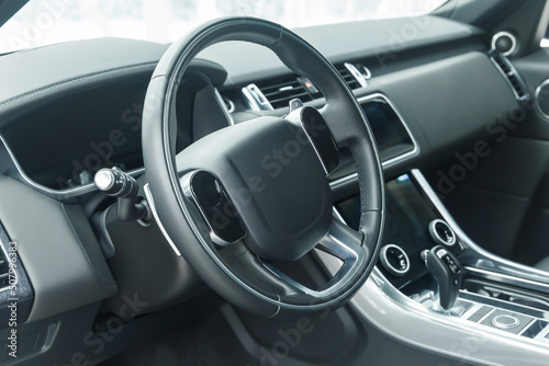 The interior of a modern car in close-up. Car interior - steering wheel, gear shift lever, multi-touch steering wheel, car control display, dashboard. Black leather. A place to copy. Without a label. © Evgenii