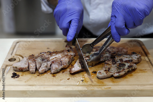 chef anónimo cortando con cuchillo y guantes carne de ternera en tabla de madera