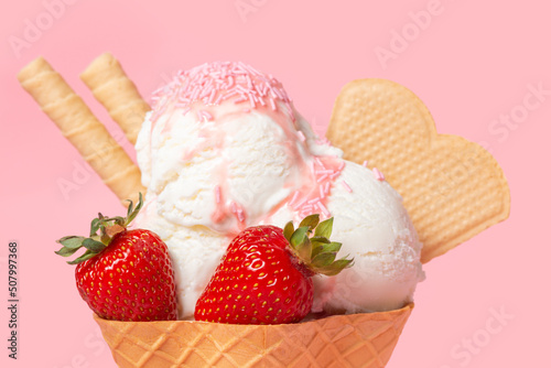 cone with scoops of ice cream strewed sprinkles, poured with glaze and decorated strawberries on pink background photo