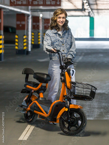 beautiful girl posing sitting on an electric scooter in the parking lot photo