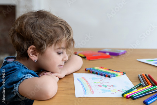 Little girl paints picture of happy family with colored pencils. Colorful child's drawing of happy mother, father and children. Concept of intimacy and togetherness.