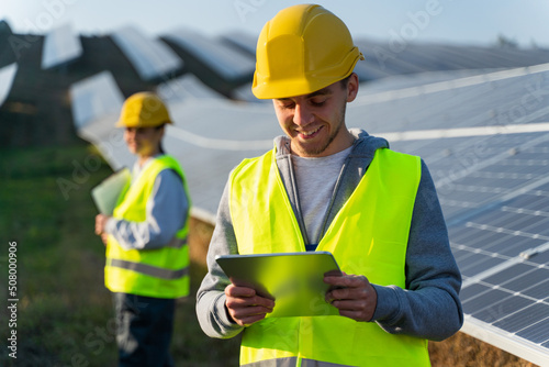 Low angle view of male engineer using tablet. Solar farm worker standing near rows with batteries. Solar panel field, clean energy production, green energy concept