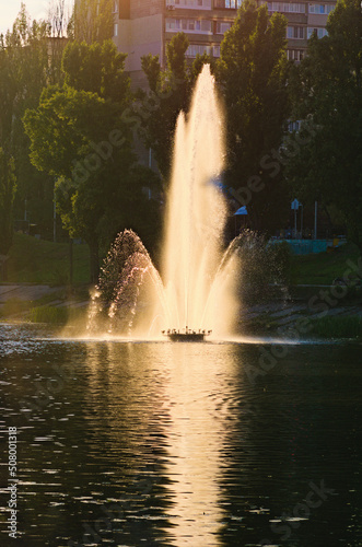 Picturesque landscape view of pond with fountain during sunset. Fountain in the city channel. Buildings of famous Rusanivka neighborhood in the background. Kyiv, Ukraine