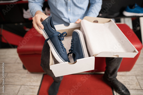 Young bearded caucasian man opens a box with shoes in a boutique, the concept of buying shoes.