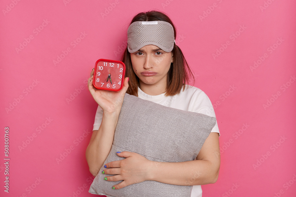 Caucasian young woman with red alarm clock and pillow awakening hard early, posing isolated on pink background, having no enough sleep, want more rest at weekends. Caucasian young woman with red alarm clock and pillow awakening hard early, posing isolated on pink background, having no enough sleep, want more rest at weekends.